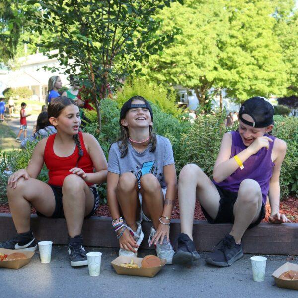 Three tweens laugh while eating lunch outside during cookout