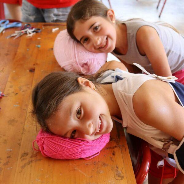 Two smiling young girls rest their heads on spools of yarn
