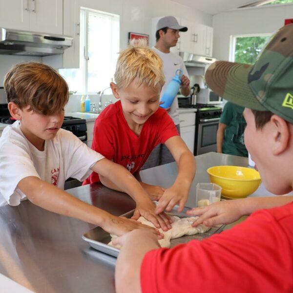 3 boys kneading a dough on a metal tray