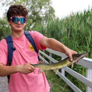teenager boy in a pink shirt holding a fish