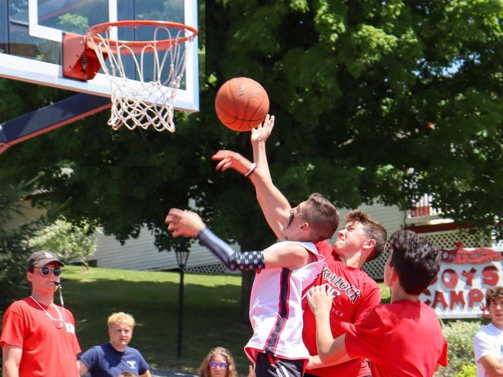 Teen boy jumps toward basket with ball in hand with defenders all around.