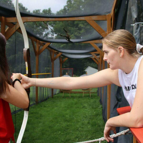 Counselor assists camper in archery class