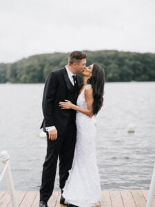 2 newlyweds kissing in front of a lake