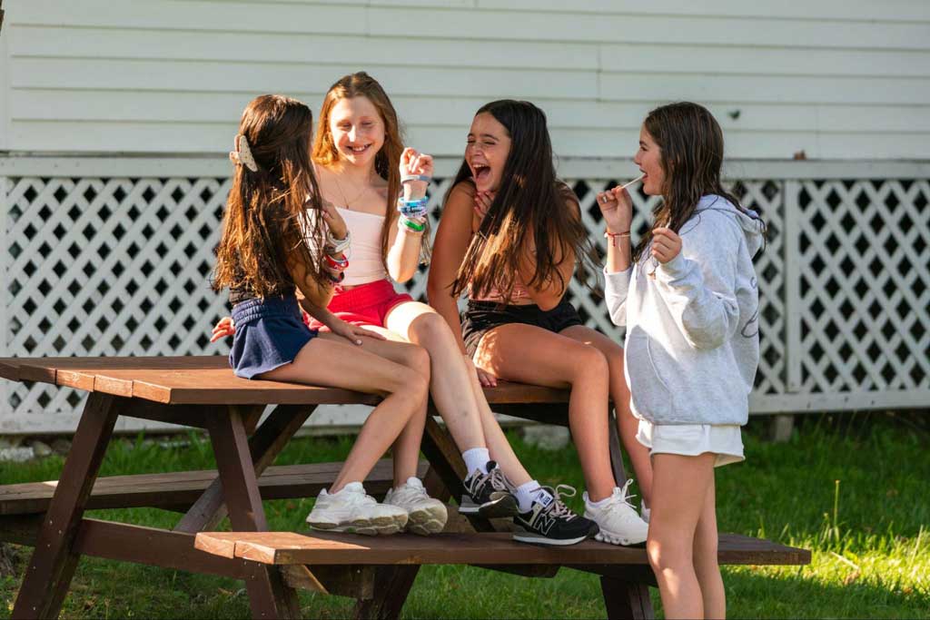 Four girls laughing and sharing around a picnic table