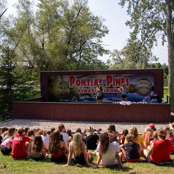 Campers seated outdoors on the grass in front of stage